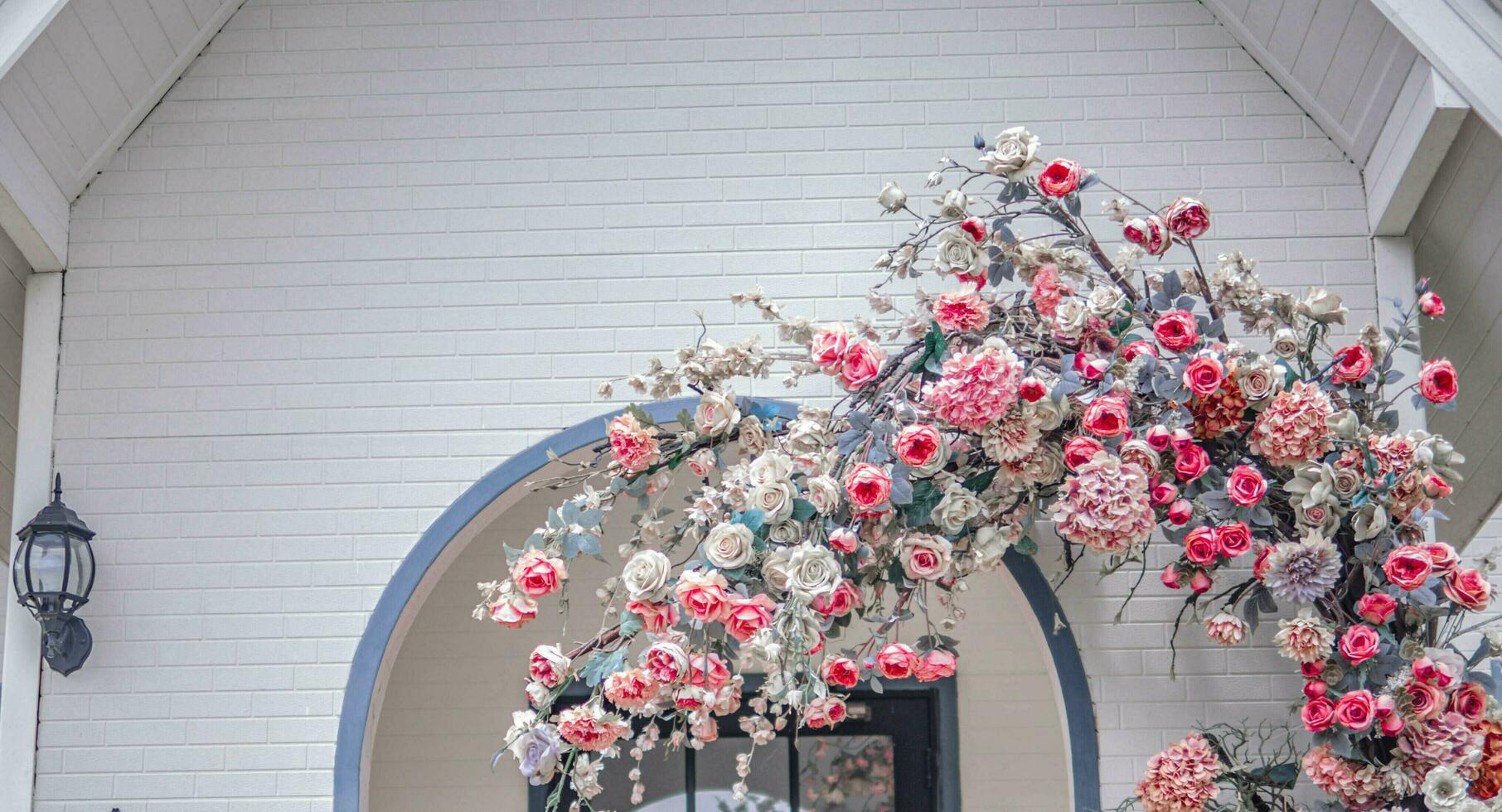 Beautiful view of the cozy house with an arched entrance covered in pink and red flowers. photo