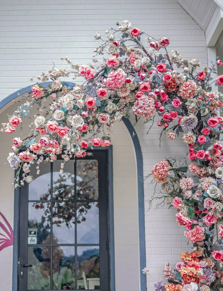 Beautiful view of the cozy house with an arched entrance covered in pink and red flowers. photo