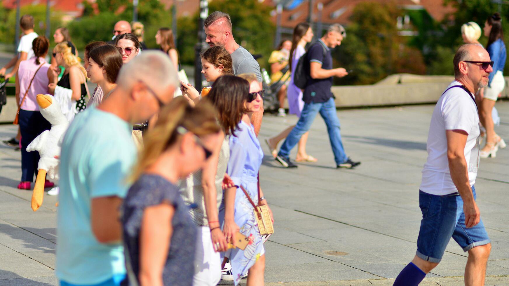 Warsaw, Poland. 29 July 2023. Crowd of people walking on a street. A crowd moving against a background of an urban old city landscape. photo