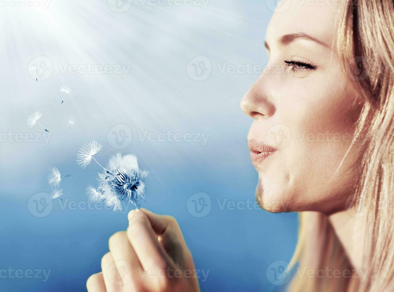 Happy beautiful girl blowing dandelion photo