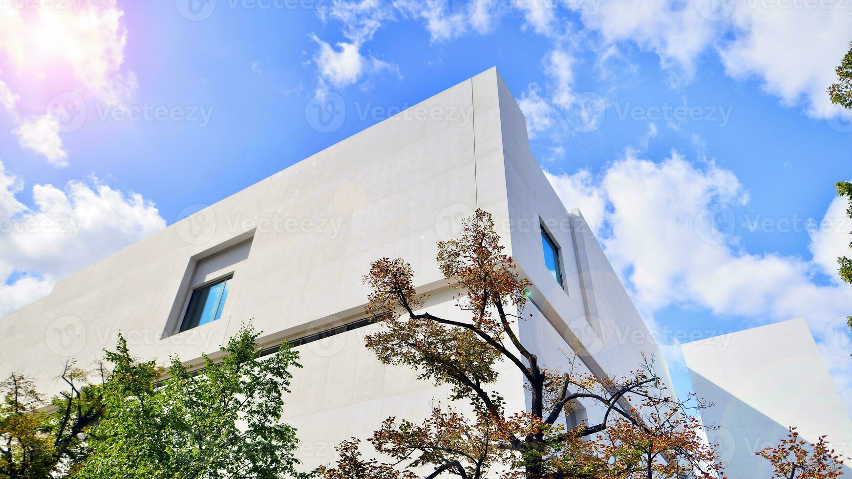 Modern white concrete building walls against blue sky. Eco architecture. Green trees and concrete office building. The harmony of nature and modernity. photo