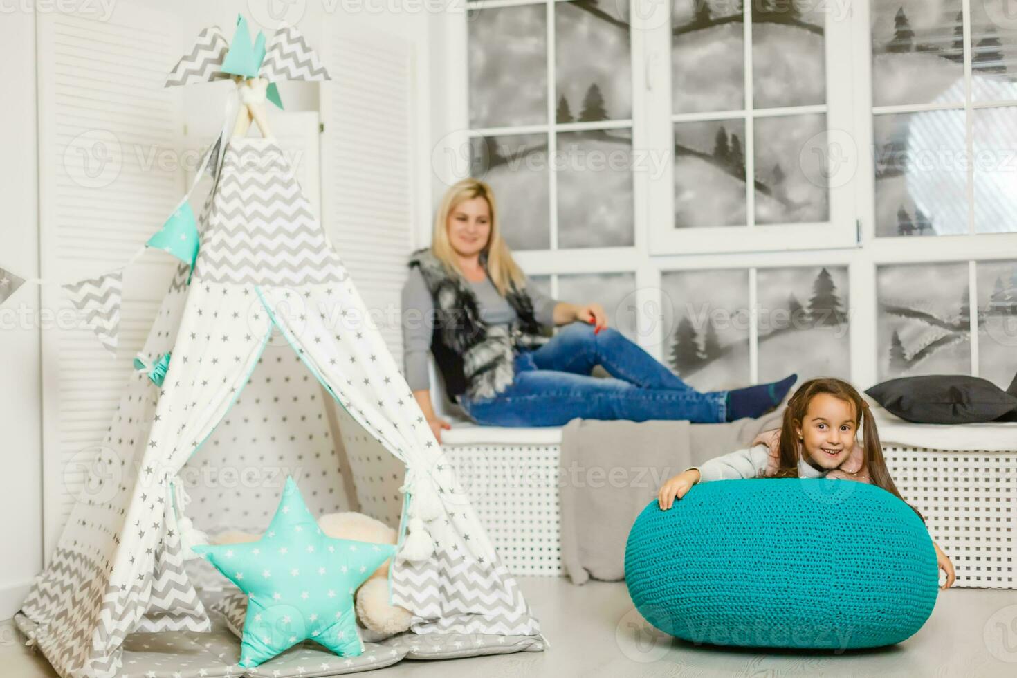 A young mother in a gray sweater and daughter are sitting in the children's room in winter. the Christmas and New Year's interior. Holiday. Family concept. photo