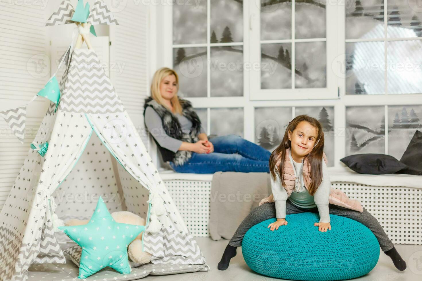 un joven madre en un gris suéter y hija son sentado en el para niños habitación en invierno. el Navidad y nuevo años interior. día festivo. familia concepto. foto