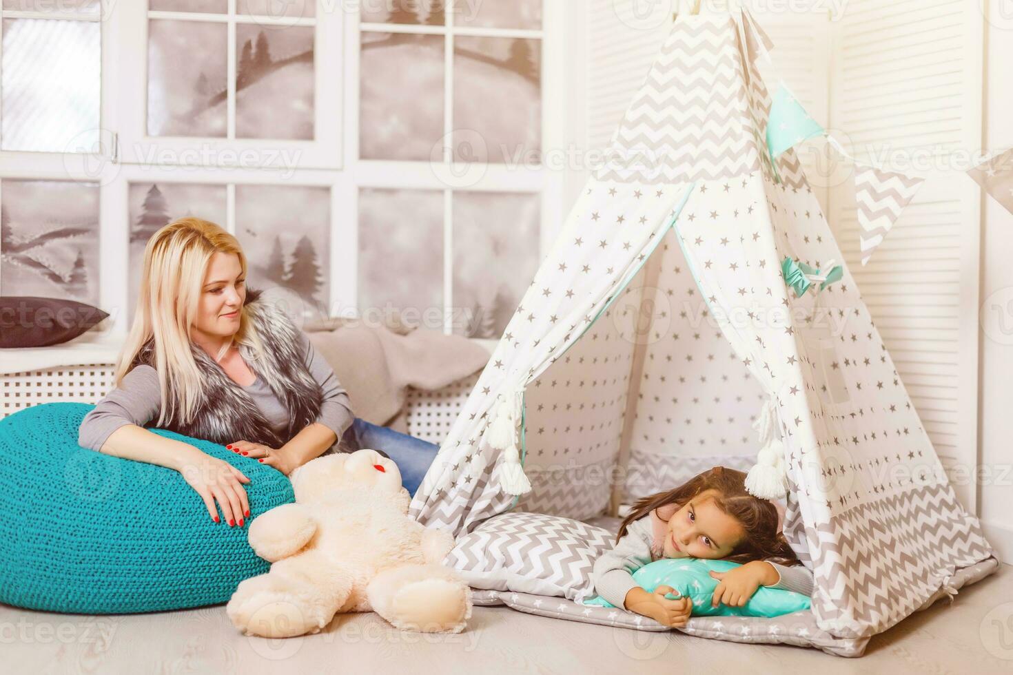 A young mother in a gray sweater and daughter are sitting in the children's room in winter. the Christmas and New Year's interior. Holiday. Family concept. photo