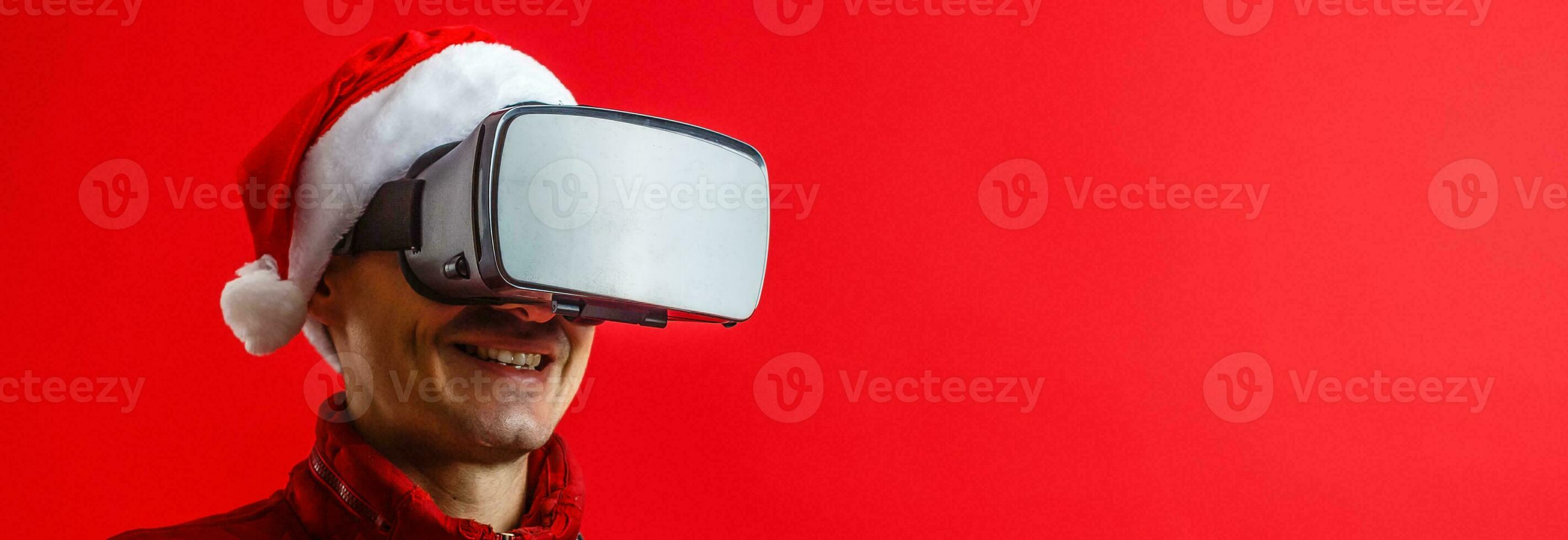 Santa Claus wearing virtual reality goggles and a red bucket with popcorn, on a red background. Christmas photo