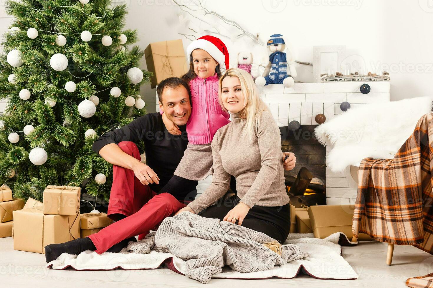 New Year. Christmas. Family. Young parents and their little daughter in Santa hats are spending time together near the Xmas tree at home photo