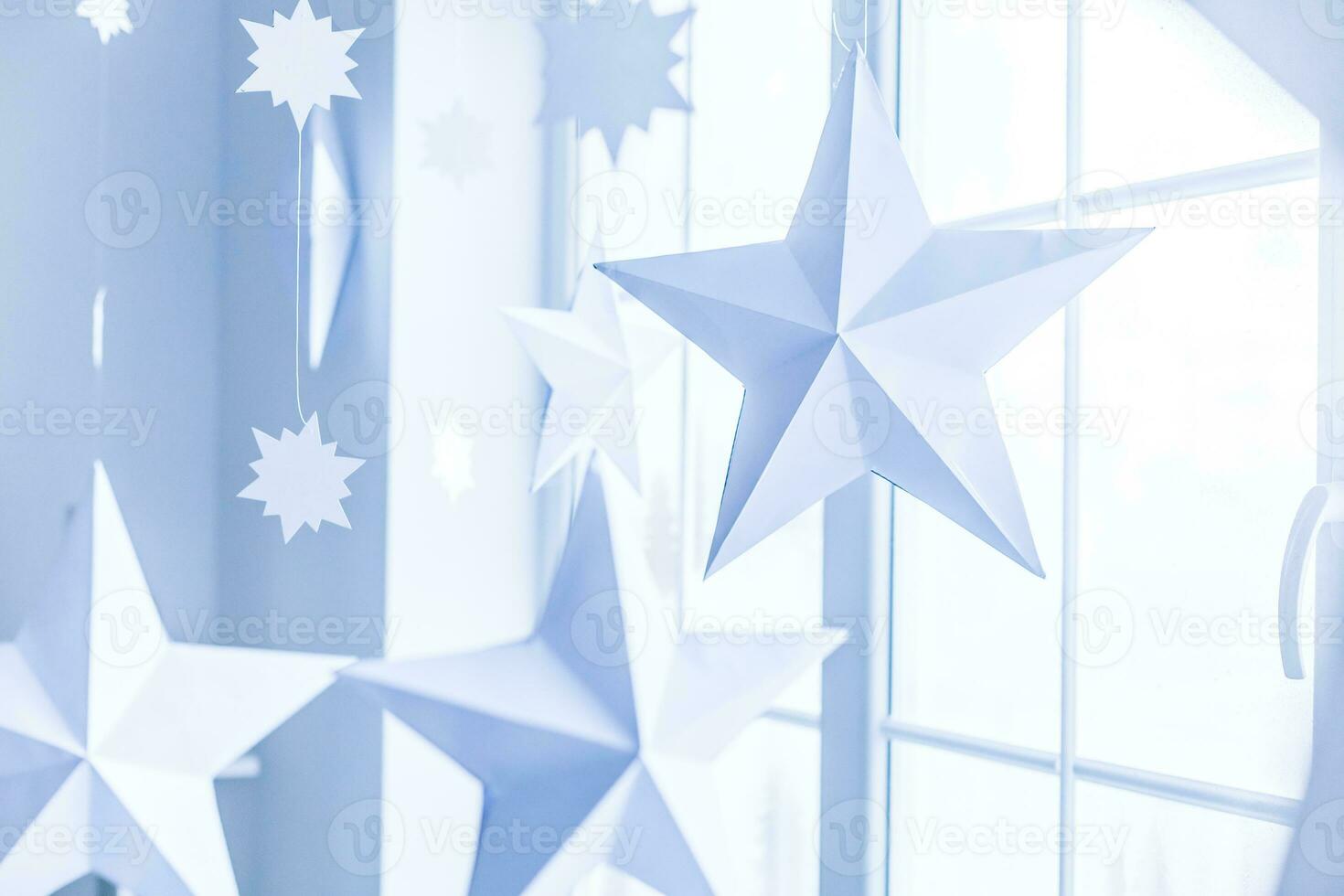 Large bright window. On the window-sill is a gray knitted plaid with gifts and sparkles with herlands. Paper Christmas stars are suspended on the background of the window. photo