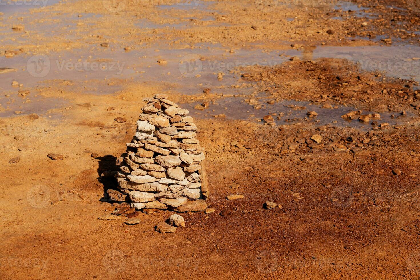 Muddy ground with spring water, with stacks of stones on one side. photo