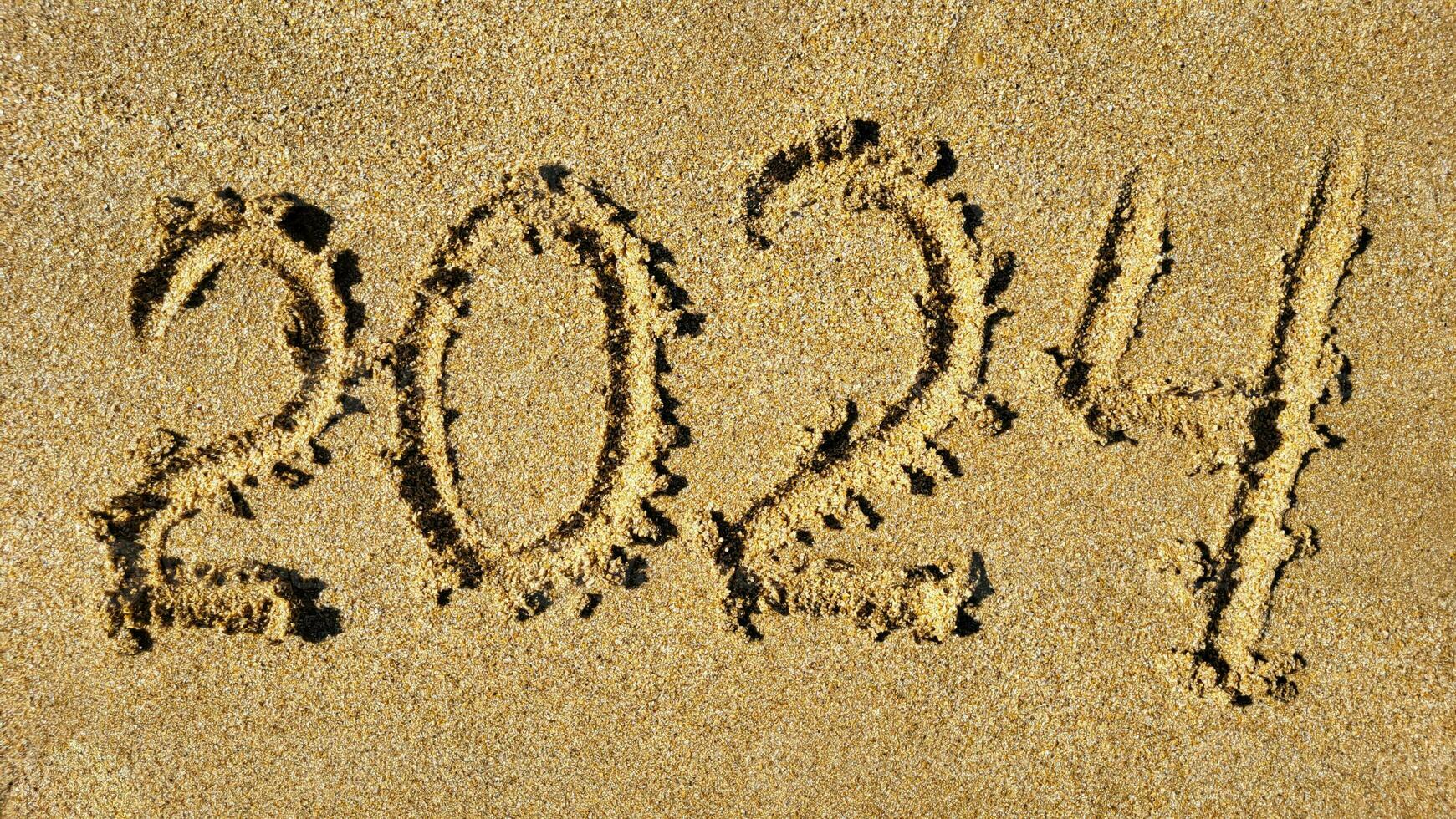 The numbers 2024 are written on the sandy beach. The concept of the new year photo