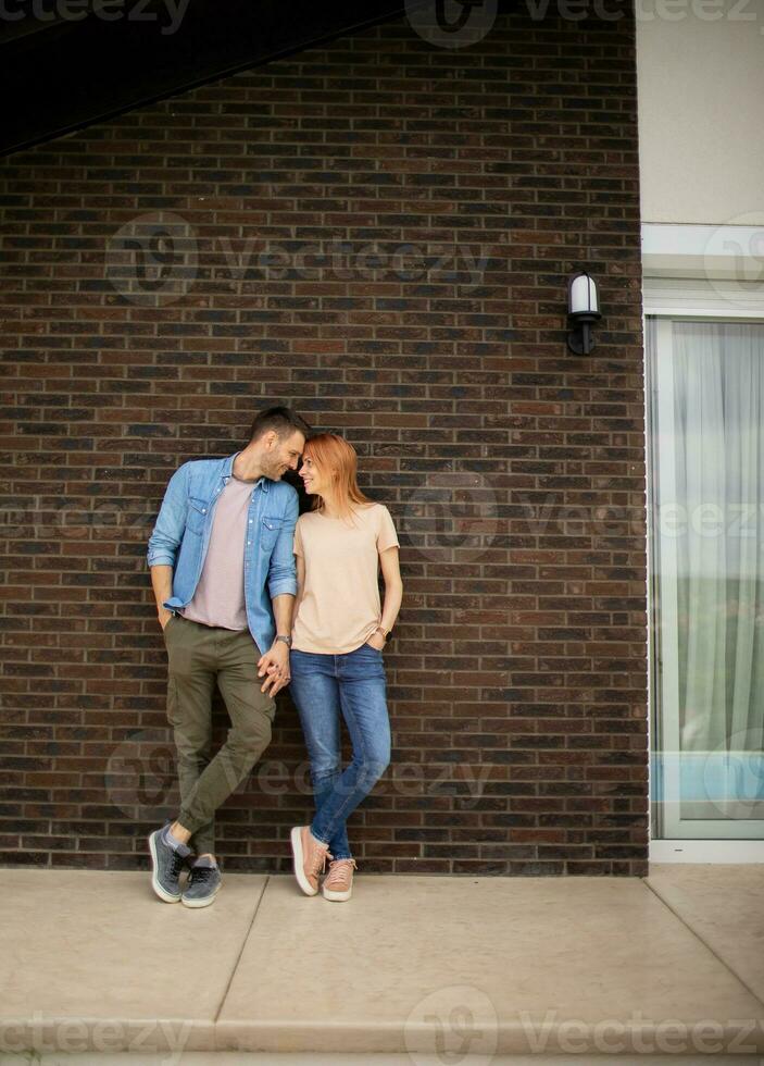 Smiling young couple in love in front of house brick wall photo