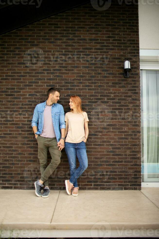 Smiling young couple in love in front of house brick wall photo