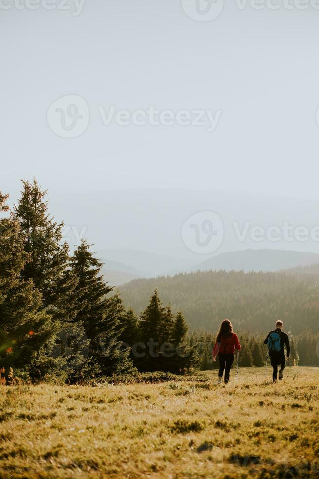 Smiling couple walking with backpacks over green hills photo