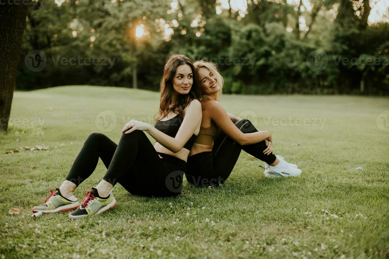 Two pretty young women sitting on grass and relaxing after outdoor training photo