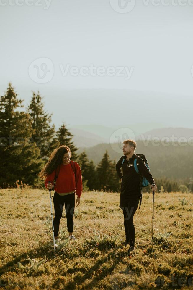 Smiling couple walking with backpacks over green hills photo