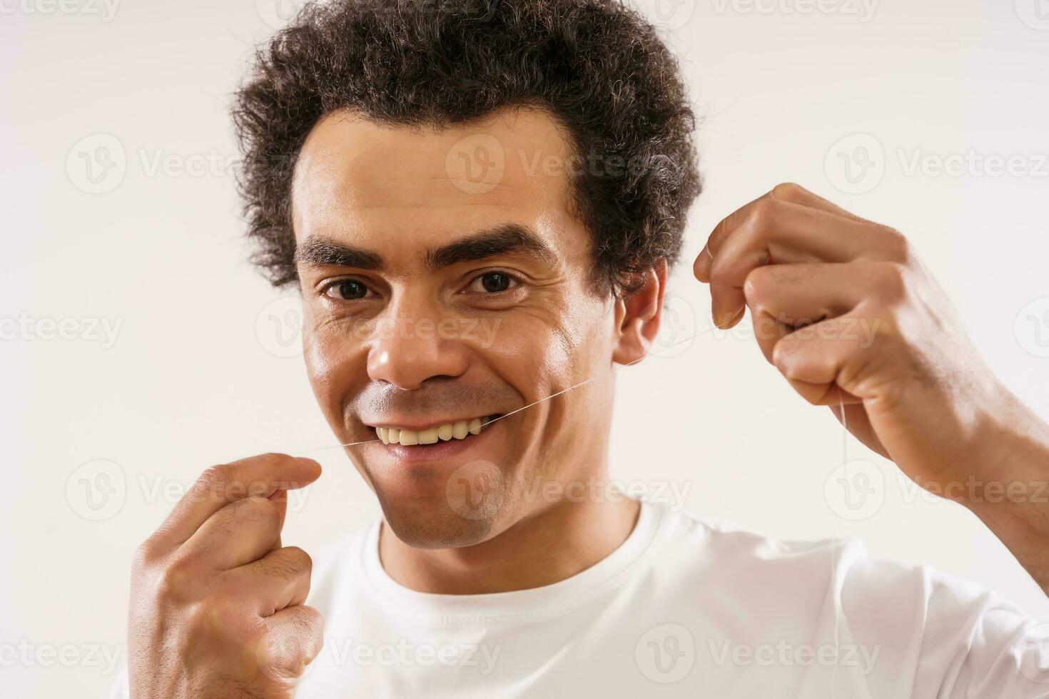 Handsome mixed race adult man is using dental floss to clean his teeth. photo