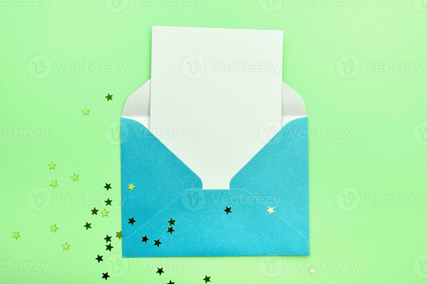 Blue open envelope with a white sheet on a green background with glitter stars. Place for your text photo