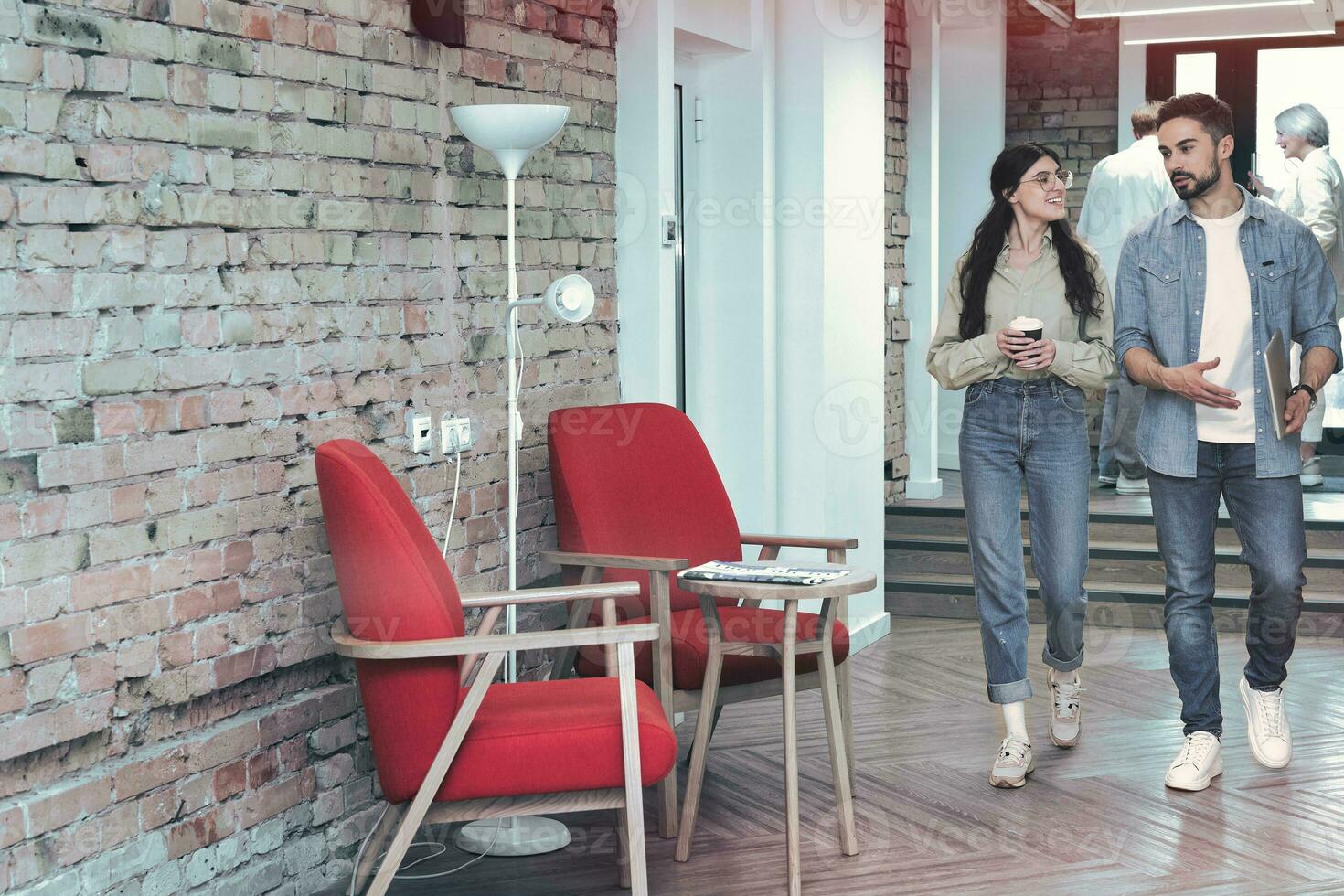 Full-length photo of two happy colleague walking in the coworking space while talking. Man with laptop, woman with coffee. Copy space