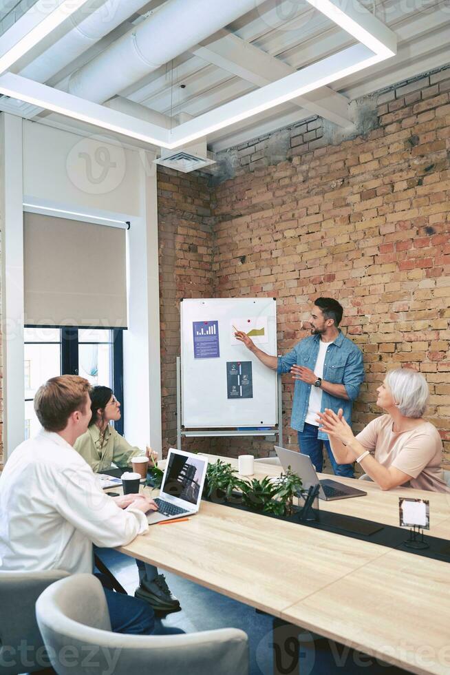 Man standing near a flipchart and talking about a new project to colleagues during a meeting in the office. Startup, coworking, management concept photo