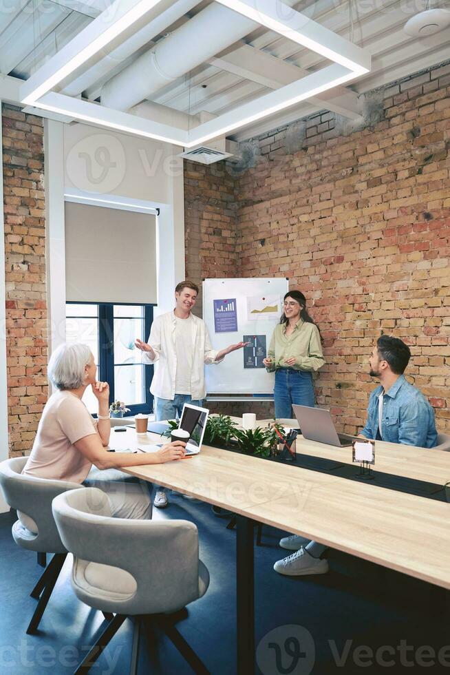 Smiling two managers presenting a new project while standing near a flipchart and speaking with colleagues in modern meeting room photo