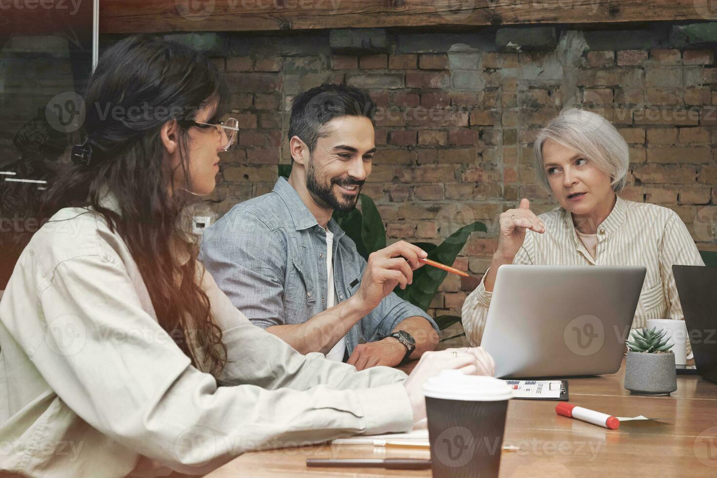 Happy young man looking at laptop screen while discussing a new idea with colleagues in meeting room. Startup, coworking, management concept photo