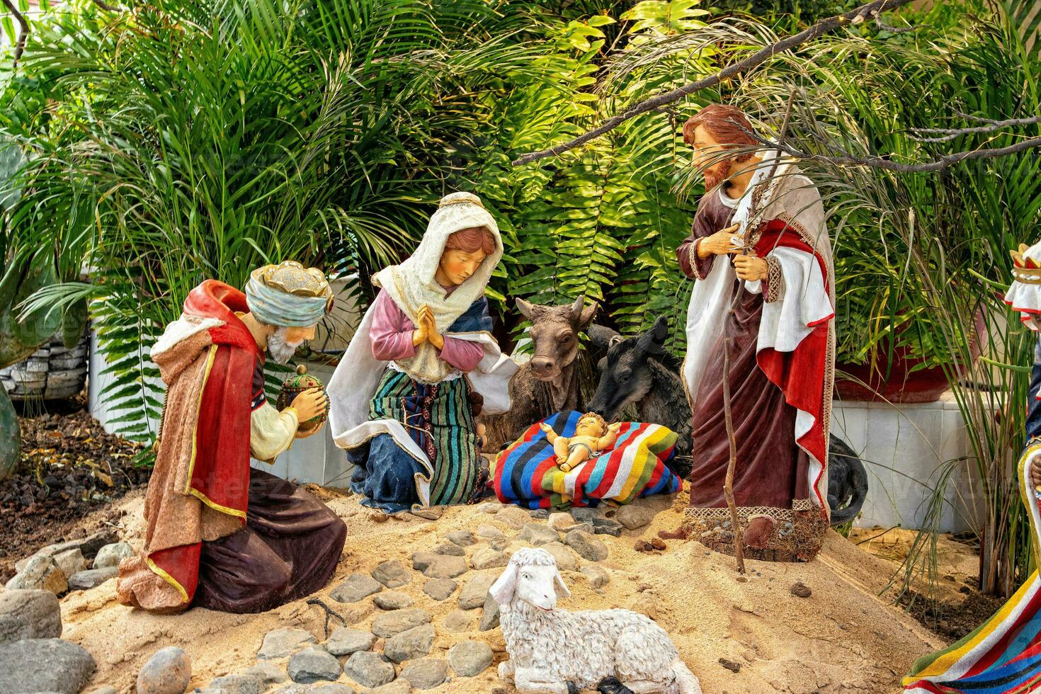 Christmas nativity scene surrounded by green palm leaves with ceramic figurines photo