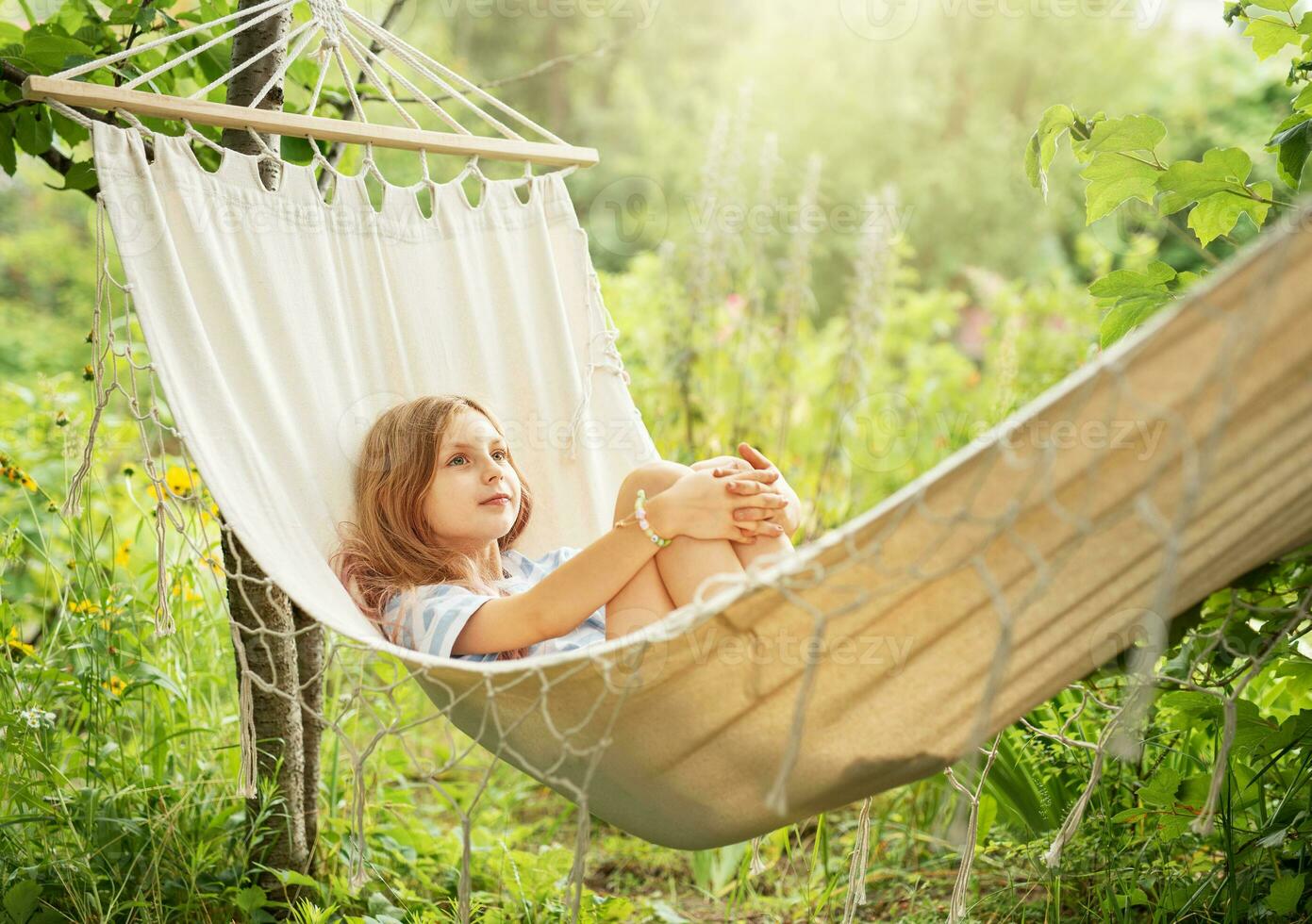 A little girl rests in a hammock and eats cherries in the summer. photo