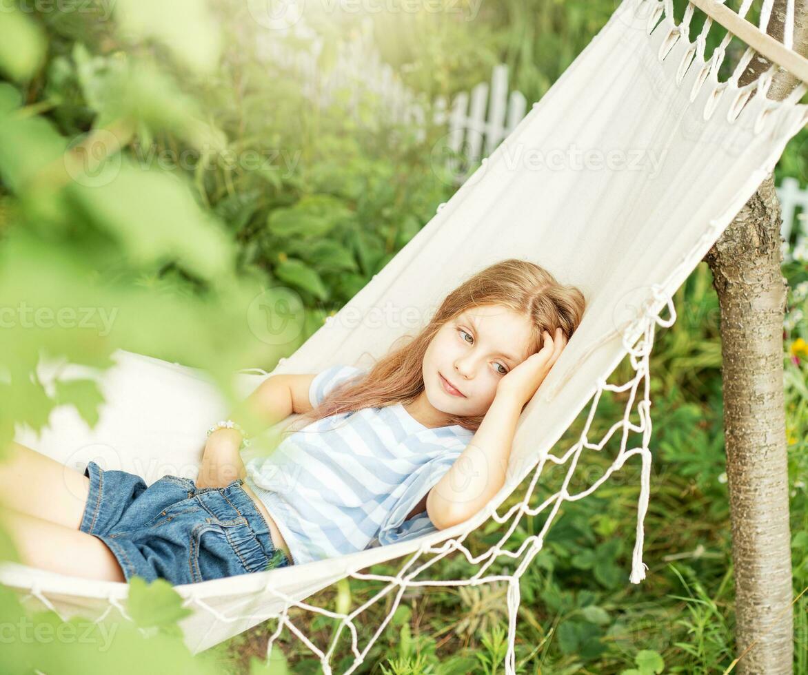 A little girl rests in a hammock and eats cherries in the summer. photo