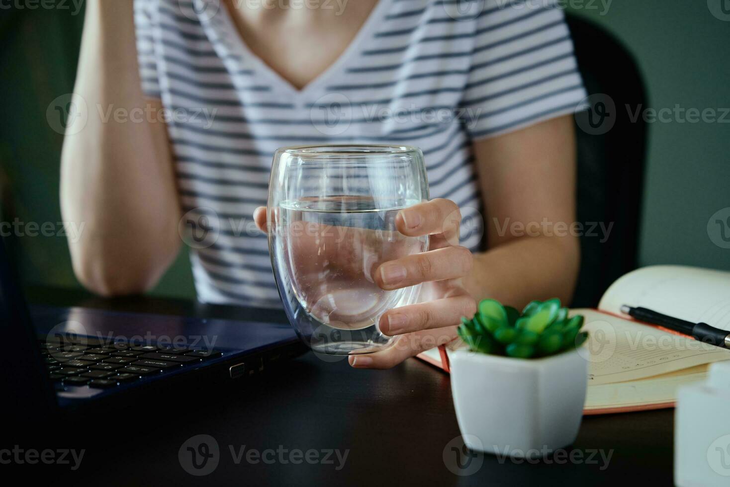 mujer sostiene vaso de agua mientras trabajos a hogar lugar de trabajo foto