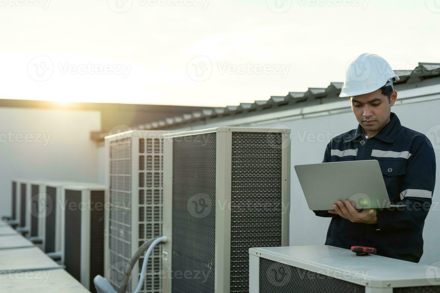 Asian maintenance engineer works on the roof of factory. contractor inspect compressor system and plans installation of air condition systems in construction. technology, online, mobile application. photo