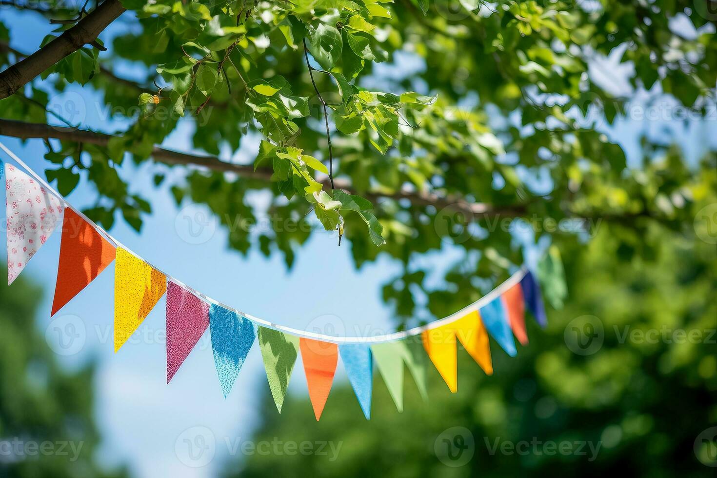 Colorful pennant string decoration in green tree foliage against blue sky summer party background with space for text photo