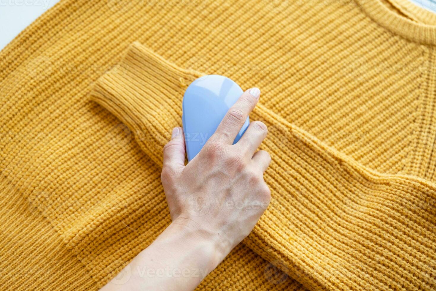 woman in yellow sweater using fabric pills removing tool photo