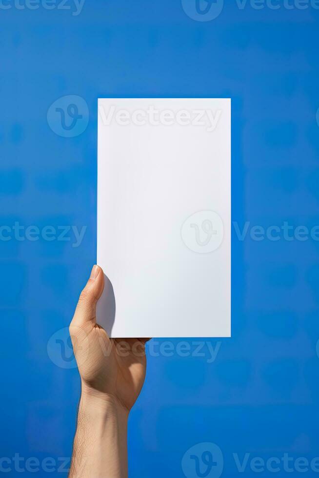 A human hand holding a blank sheet of white paper or card isolated on blue background. ai generated photo