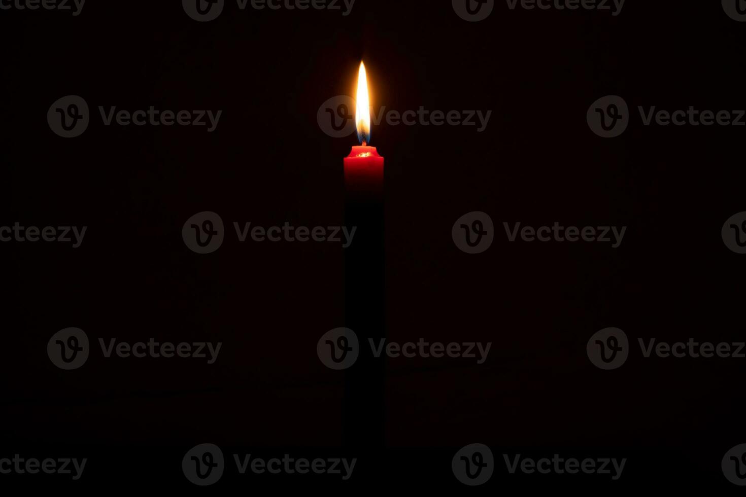 Single burning candle flame or light glowing on a small red candle on black or dark background on table in church for Christmas, funeral or memorial service with copy space. photo