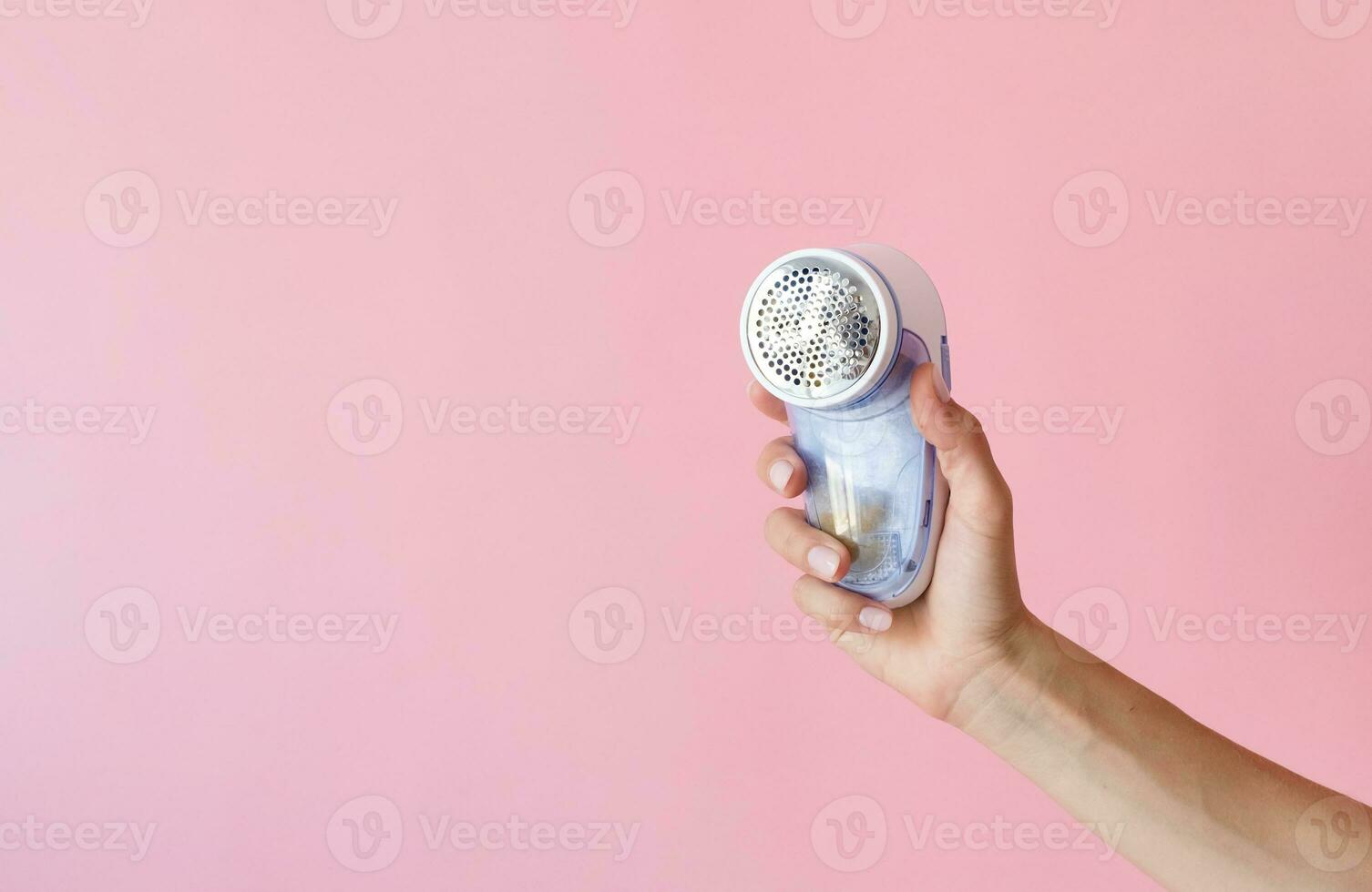 female hand holding anti-pilling razor machine on pink background photo