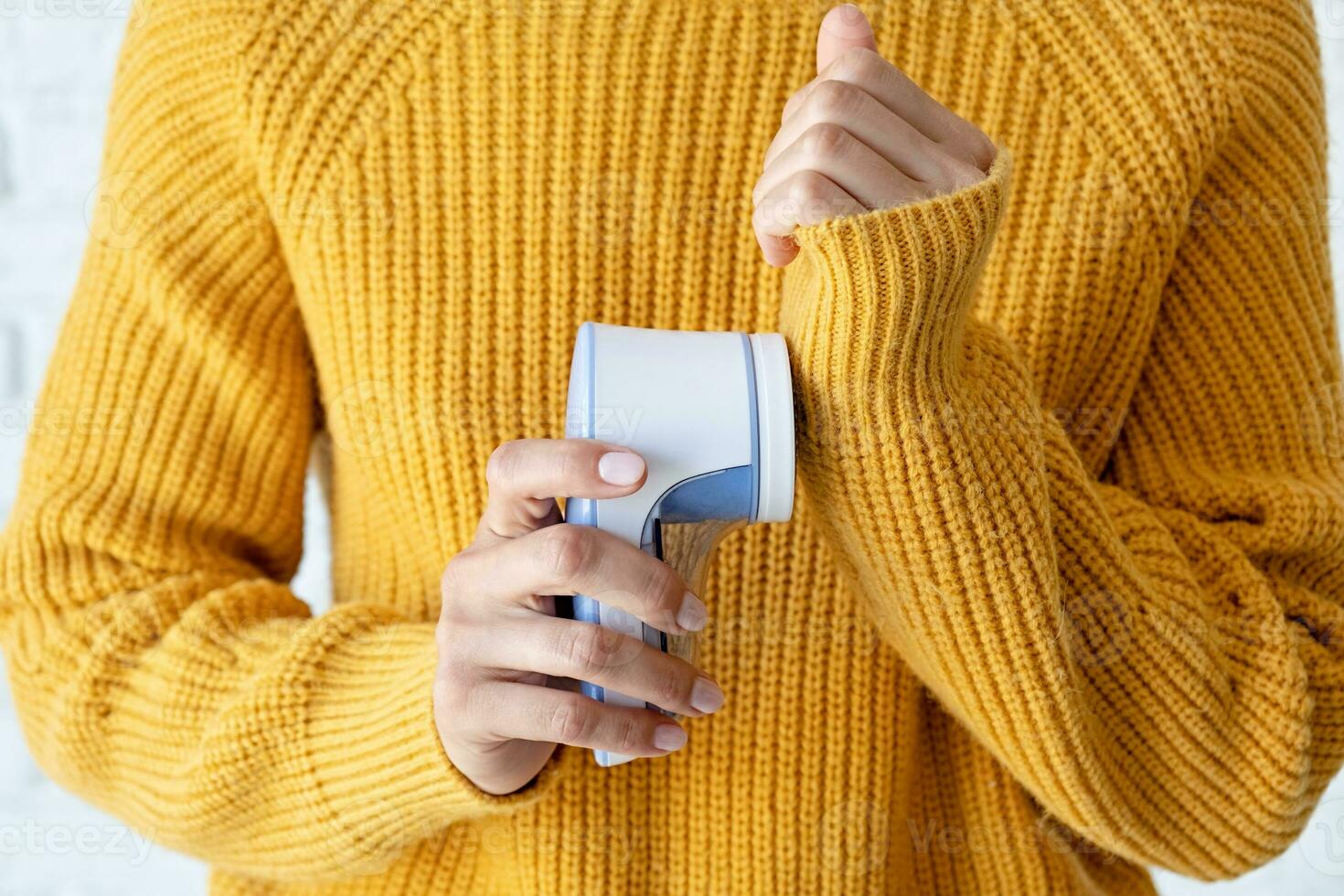 woman in yellow sweater using fabric pills removing tool photo