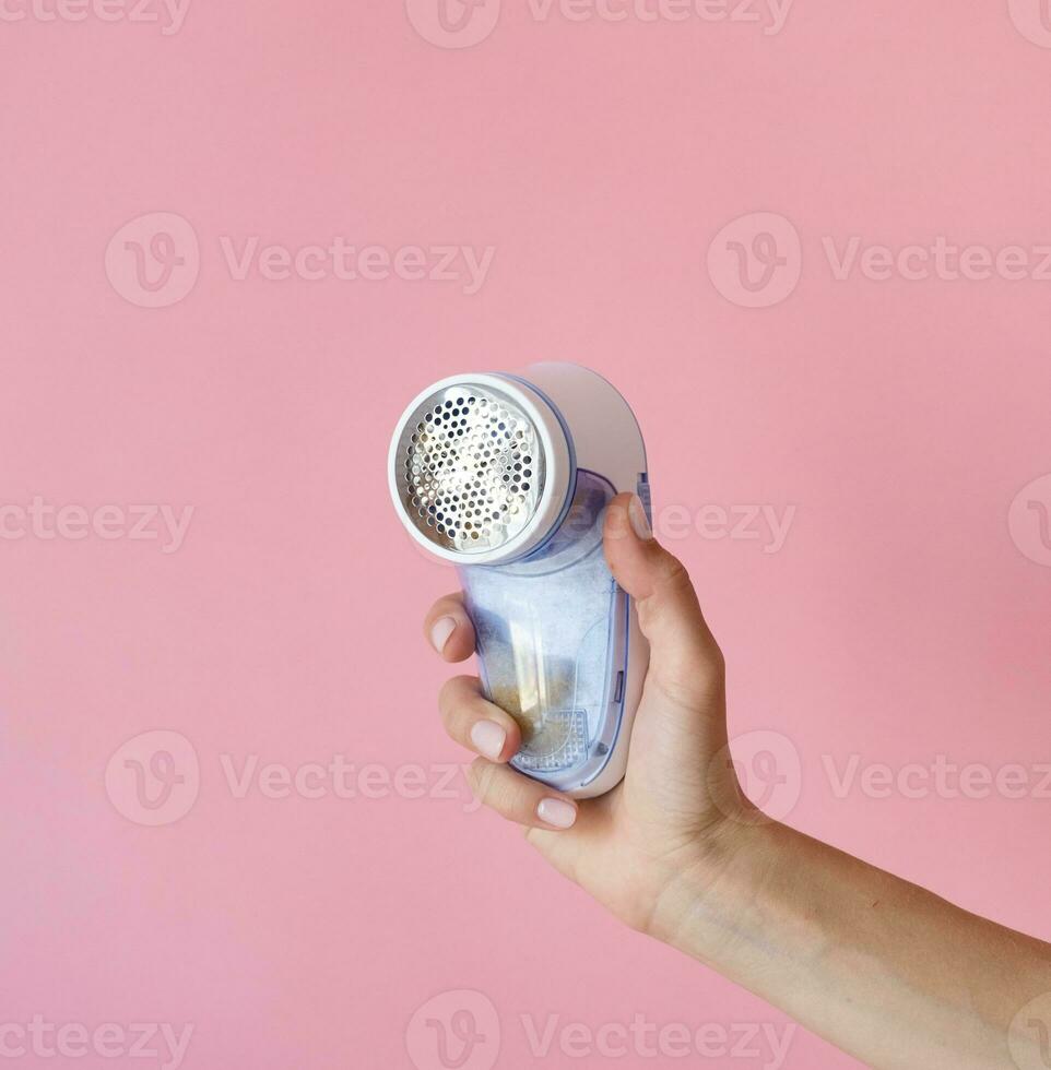 female hand holding anti-pilling razor machine on pink background photo