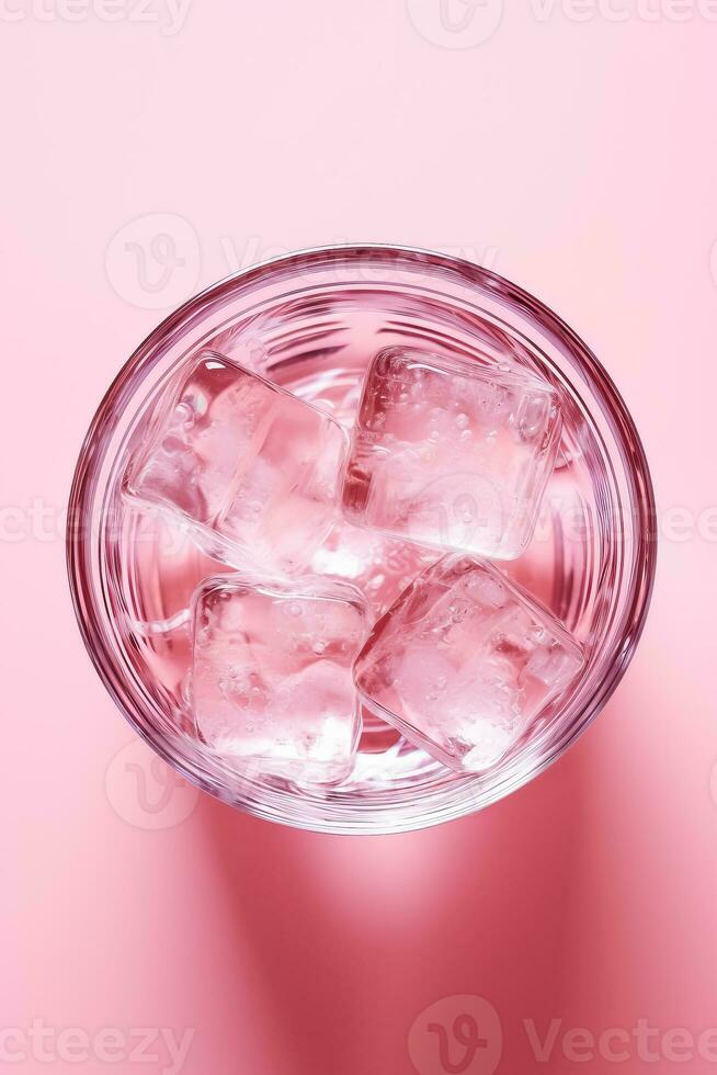 Top view of glass of water with ice on pink background isolated photo