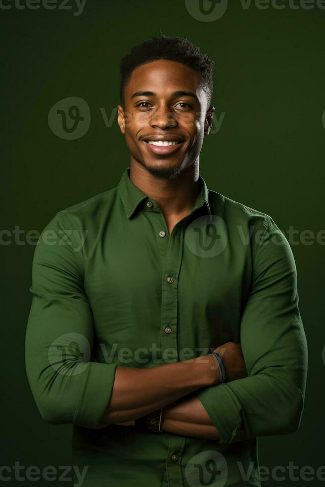 Smiling young black man stands in front of green backdrop with folded arms and green shirt photo