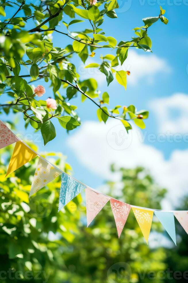 Colorful pennant string decoration in green tree foliage against blue sky summer party background with space for text photo