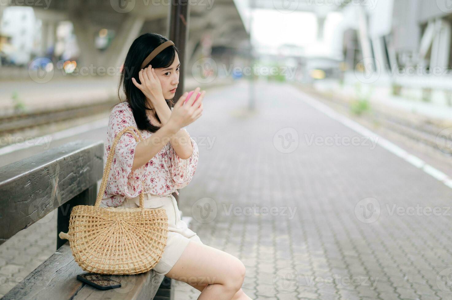 joven asiático mujer viajero comprobación su cara en un espejo y esperando para tren en tren estación. viaje viaje estilo de vida, mundo viaje explorador o Asia verano turismo concepto. foto