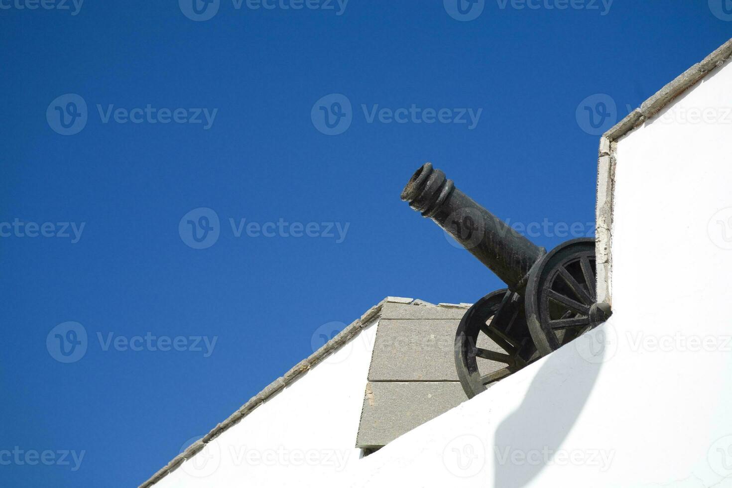 old antique black cannon on a white wall with a blue sky background photo