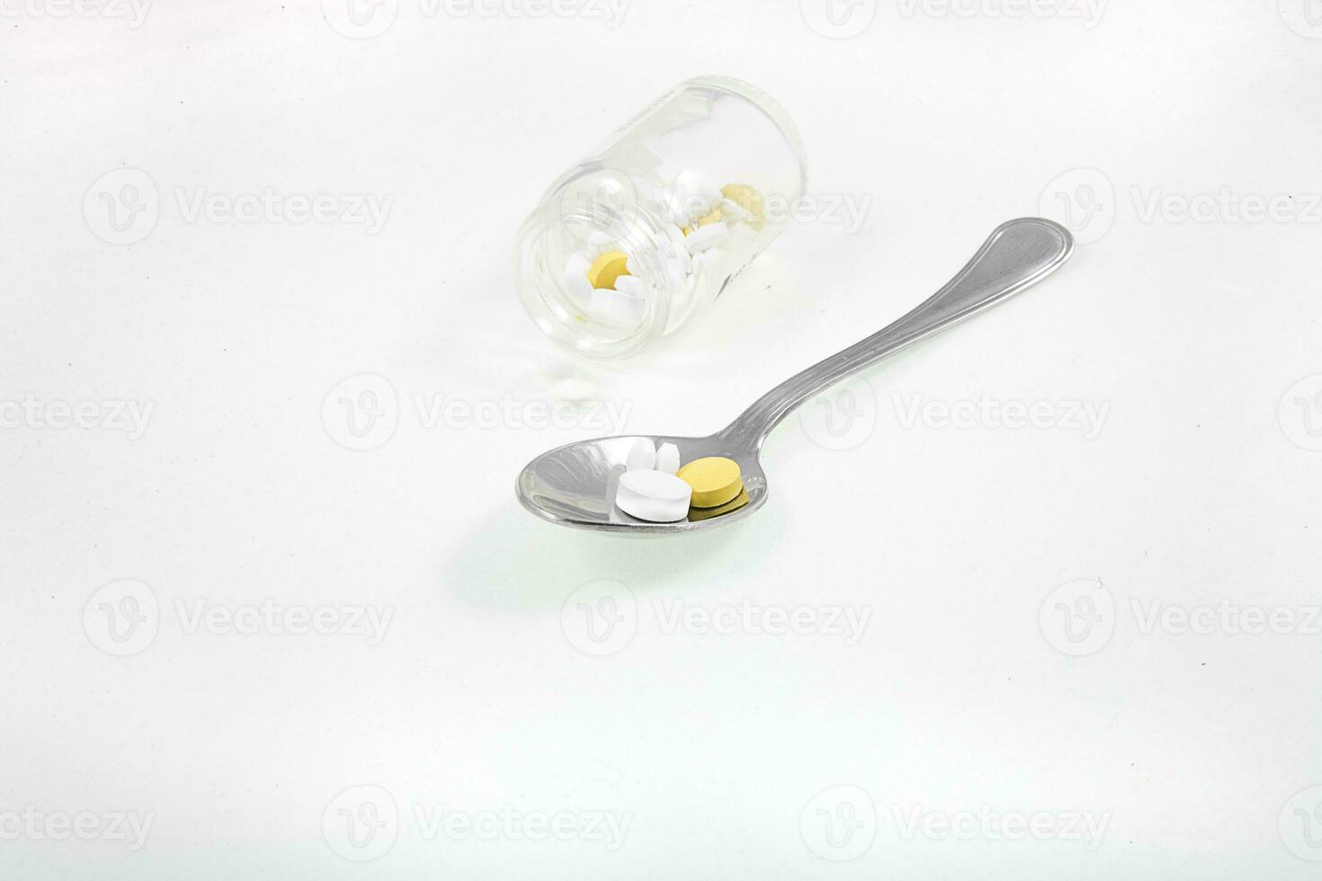 glass container and a silver spoon with medicine on a white isolated background photo