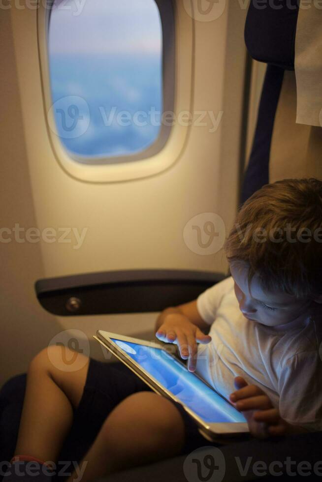 Boy spending time with tablet PC during flight photo