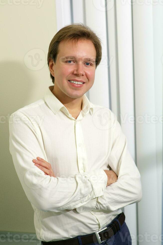 Happy young man with folded arms indoor photo