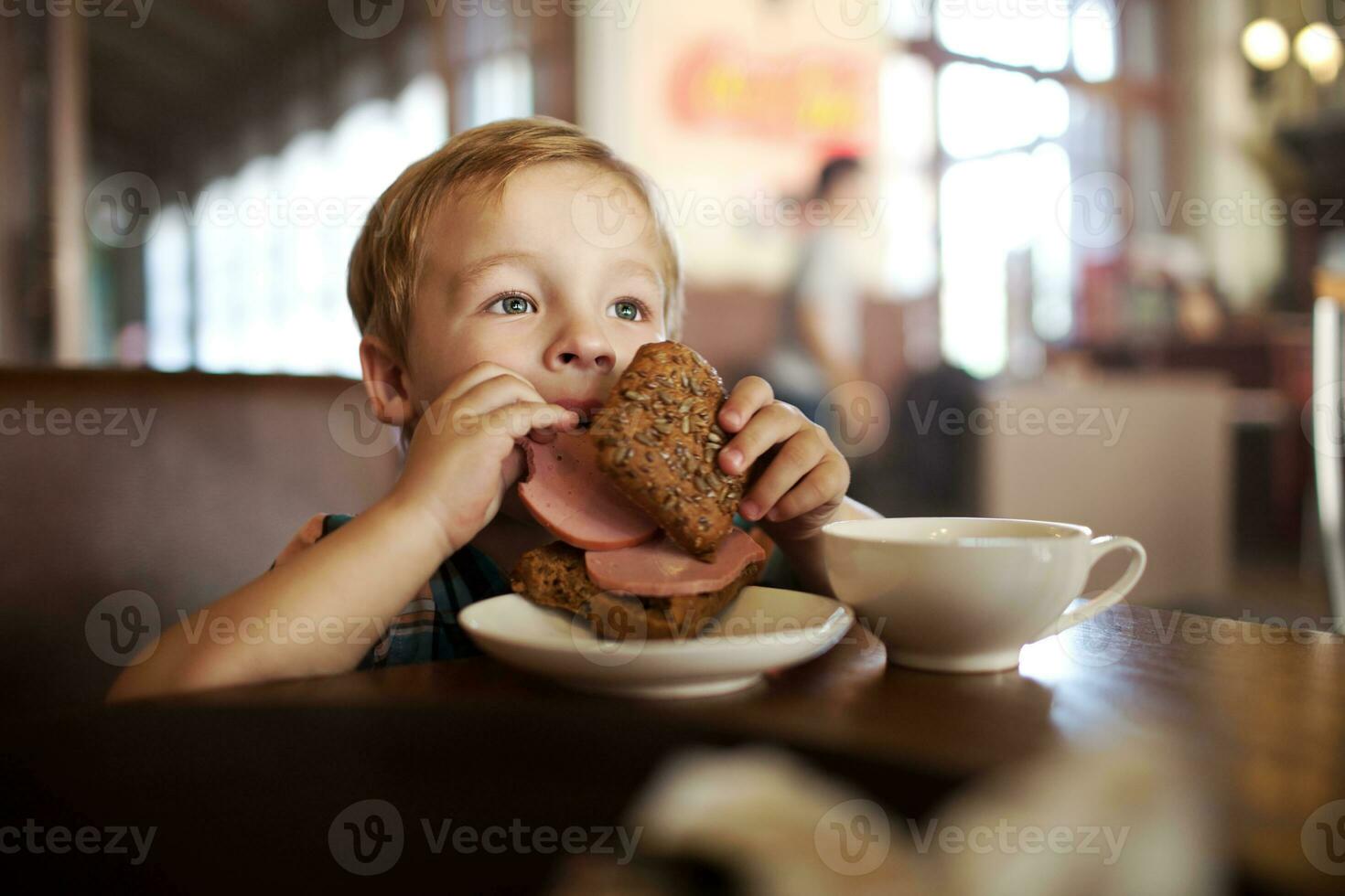 pequeño niño teniendo almuerzo con emparedado y té en café foto