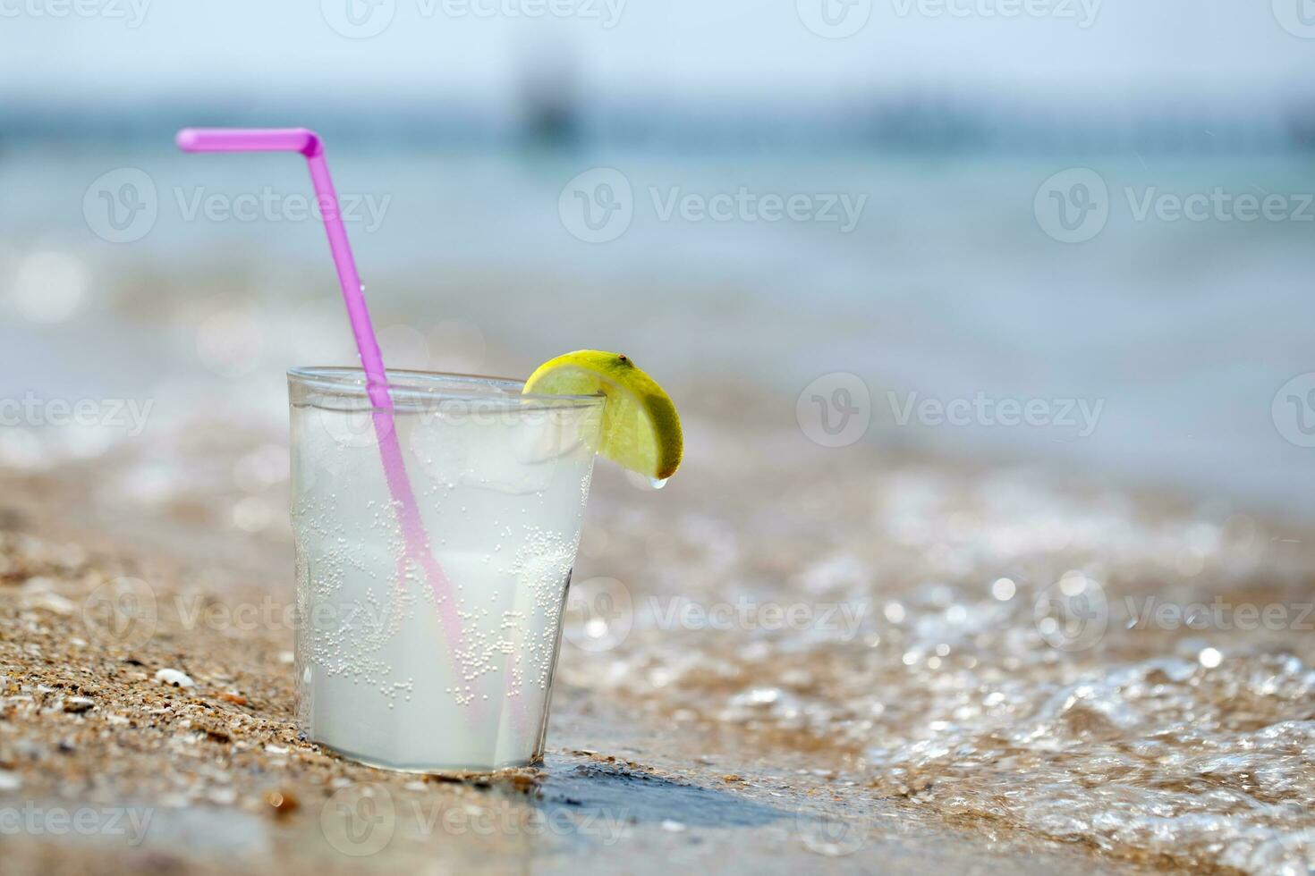 Glass of lemonade or water on beach by sea photo