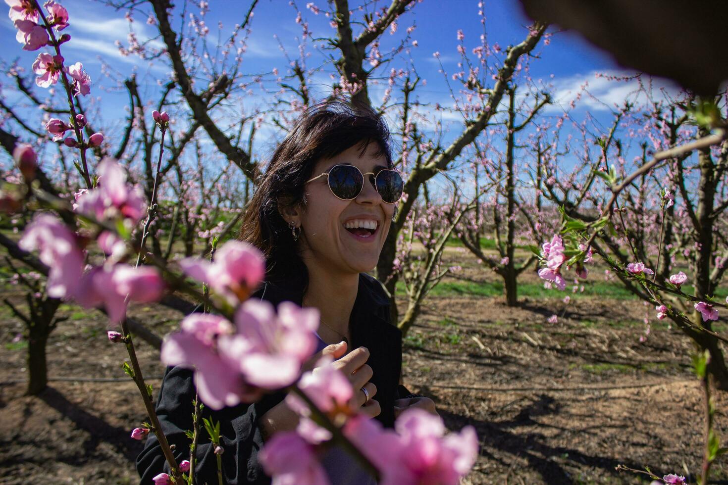 mujer sonrisas entre el bonito rosado flores de el melocotón árbol. foto