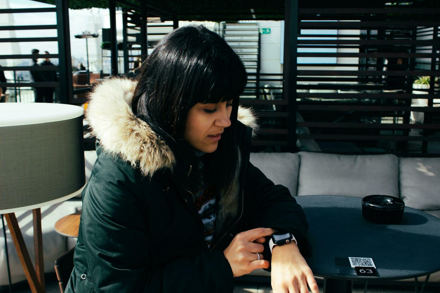 niña esperando mirando a el reloj a un mesa en el terraza de un bar foto