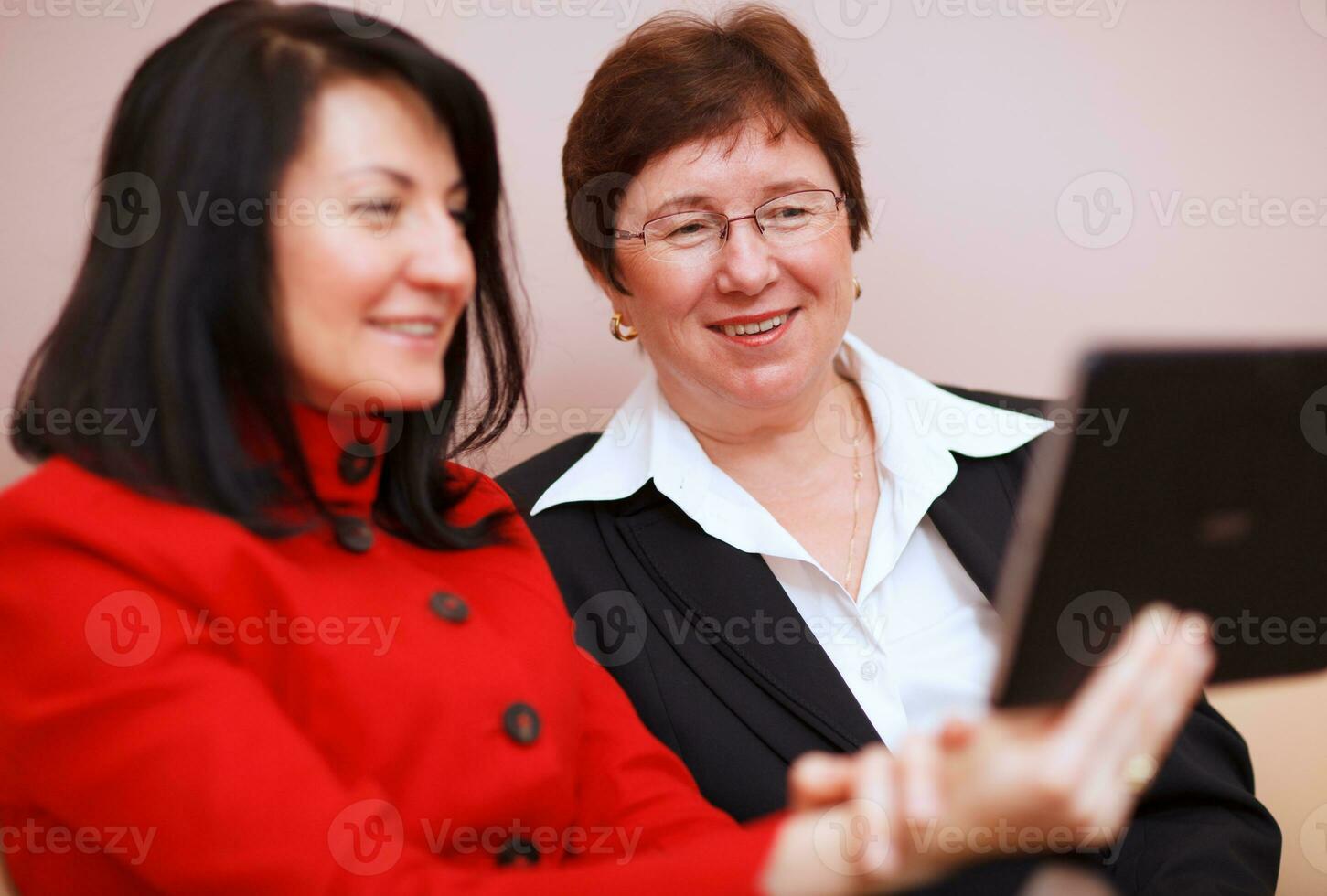 dos mujer compartiendo un tableta computadora foto