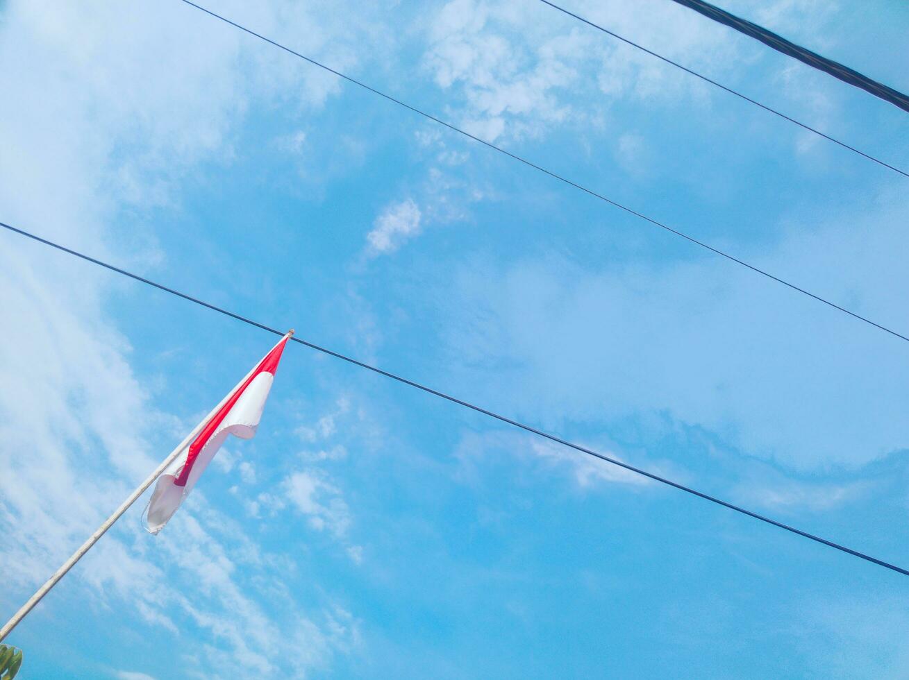 red and white flag of Indonesia against the sky and power lines in the background photo